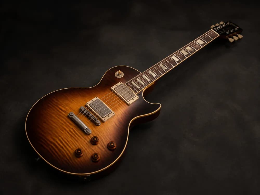 A sunburst single-cut electric guitar on a dark studio backdrop
